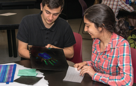 Two students at a table examine a hand print on thermographic paper.