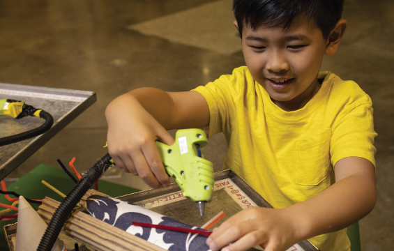 A young child uses a glue gun on a cardboard craft.
