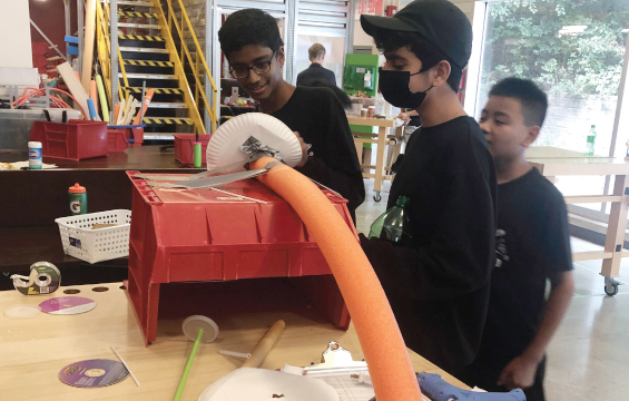 Three students work on a Rube Goldberg machine in a workshop.