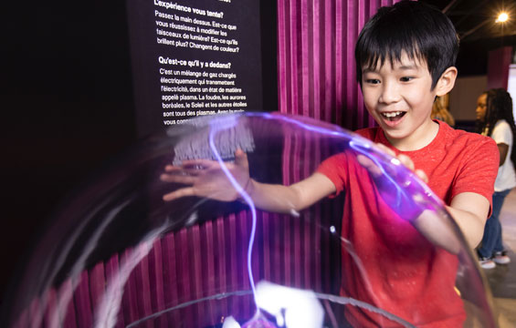 A boy with his hands on a plasma ball.