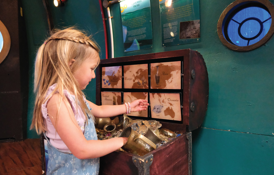 A child rummages through a treasure chest full of golden treasures.