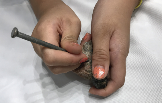 Hands using a large nail as a chisel on a rock
