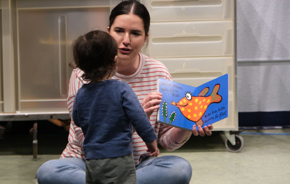 A woman reads a book to a toddler.