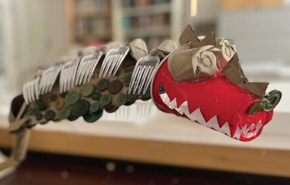 A dinosaur made of found materials including plastic forks, buttons, egg cartons and a red solo cup.