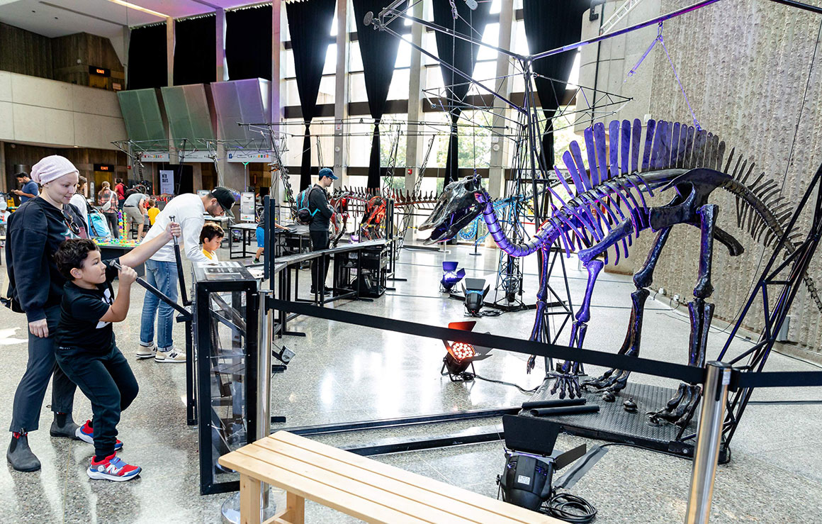 People playing with a metal dinosaur sculpture.