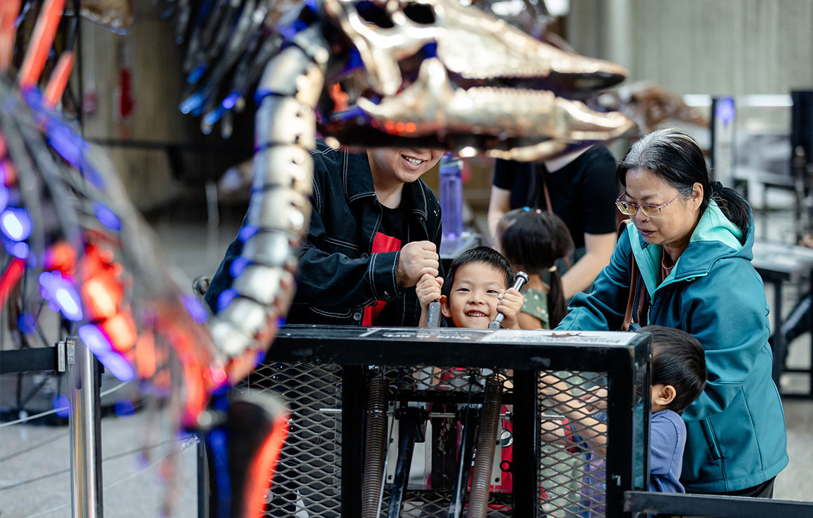People playing with a metal dinosaur sculpture.