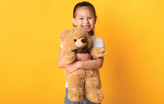 A smiling young child holds a teddy bear.