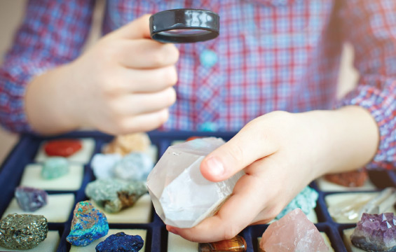 A child looks at a collection of rocks and minerals with a magnifying glass.