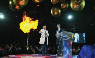 A presenter on stage creates a fireball at the end of a long stick.