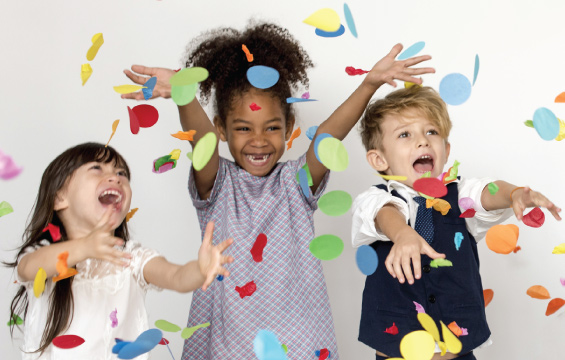 Three smiling children celebrate with confetti.