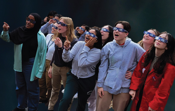 A group of students wearing eclipse glasses look up at an eclipse
