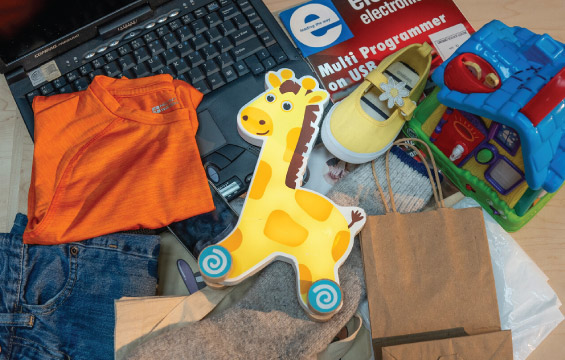 A collection of items including a toy giraffe, laptop, t-shirt, jeans, paper bag, kids' shoe, book and more.