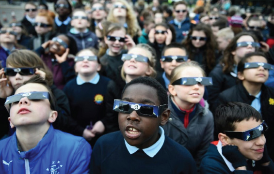 A group of middle school students look at the sky wearing eclipse glasses.