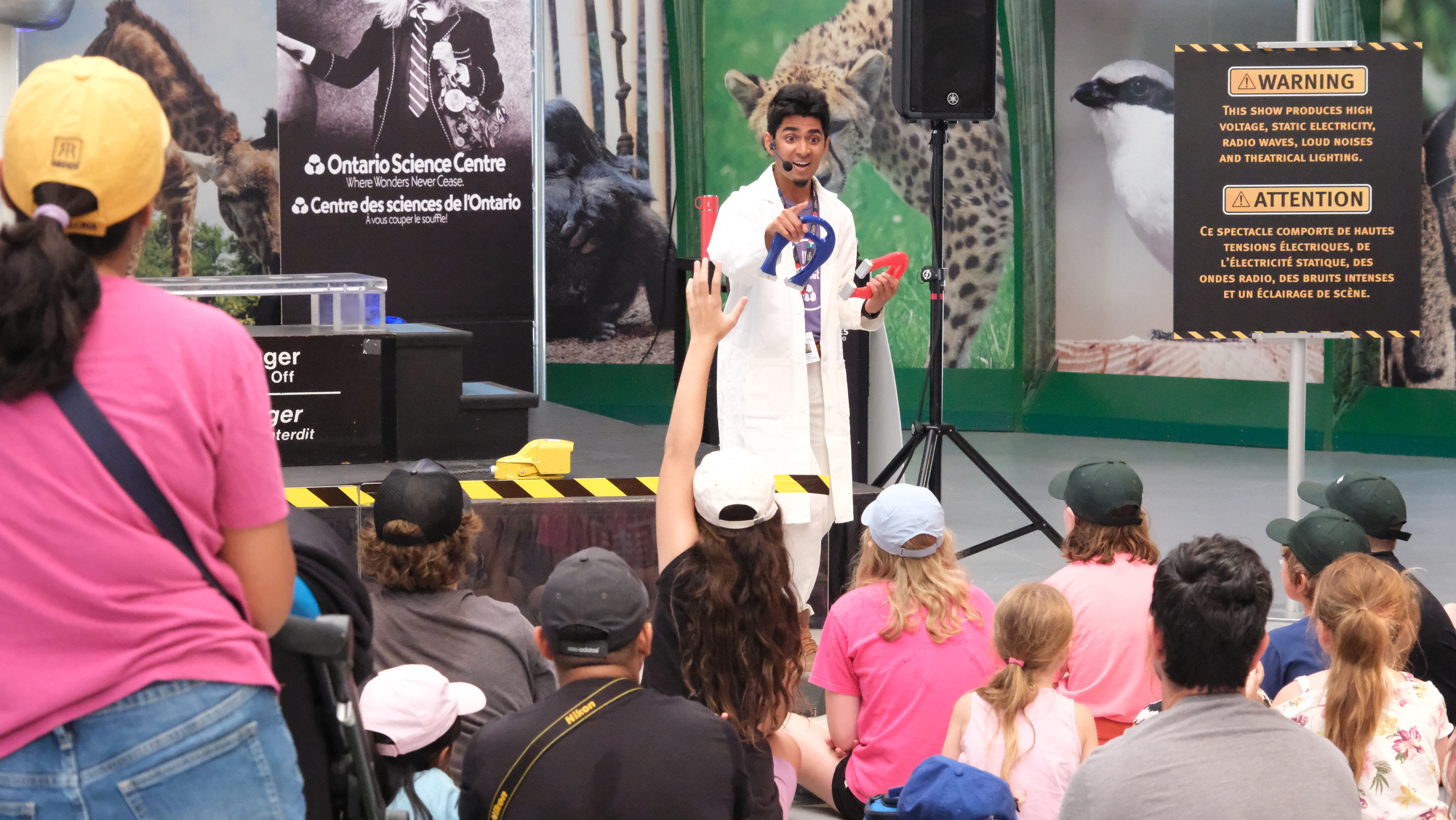 A science centre staff engages with a crowd of children.