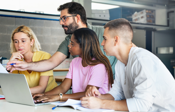 Young teacher helping teenager students near a computer.