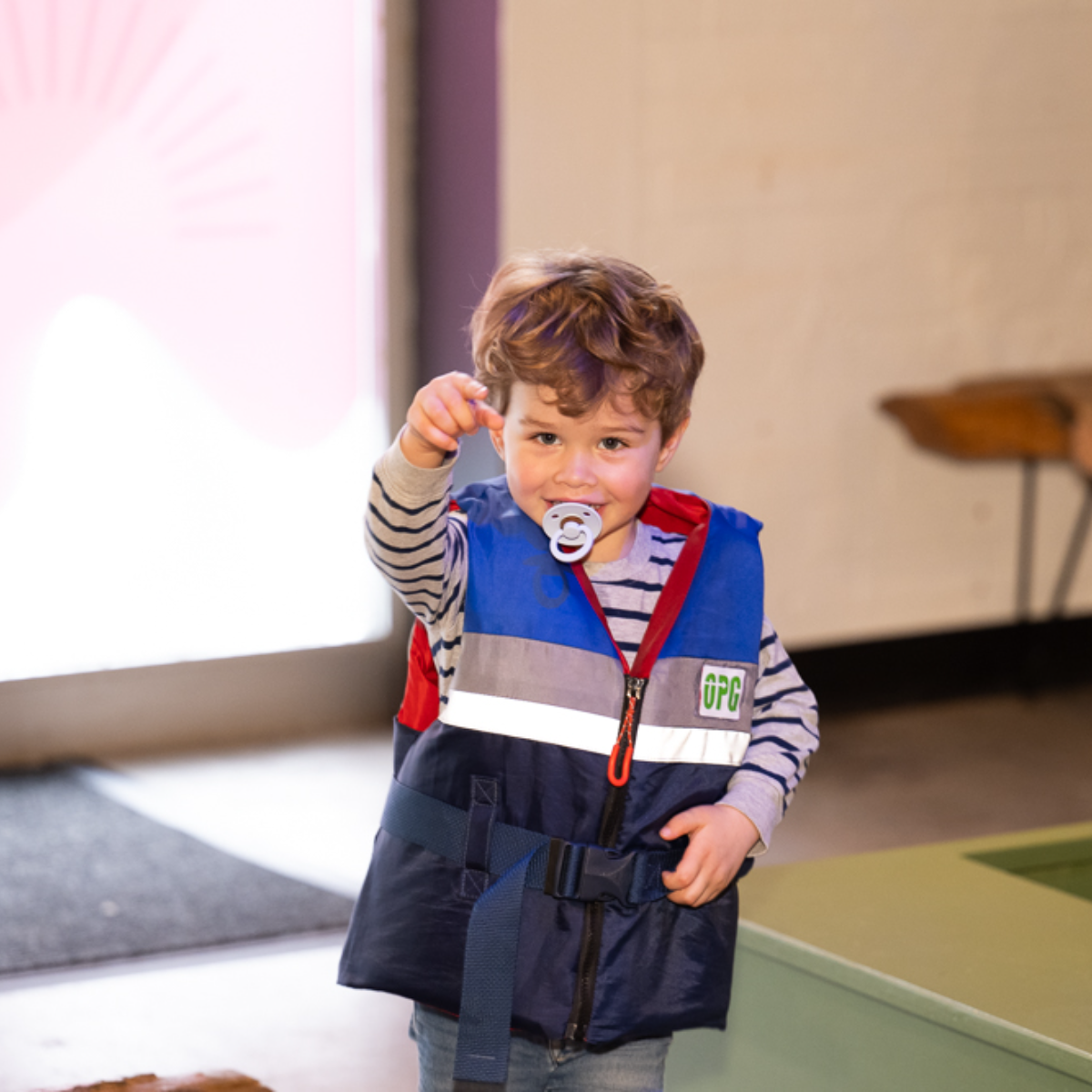 A boy wearing a life jacket pointing finger at the camera.
