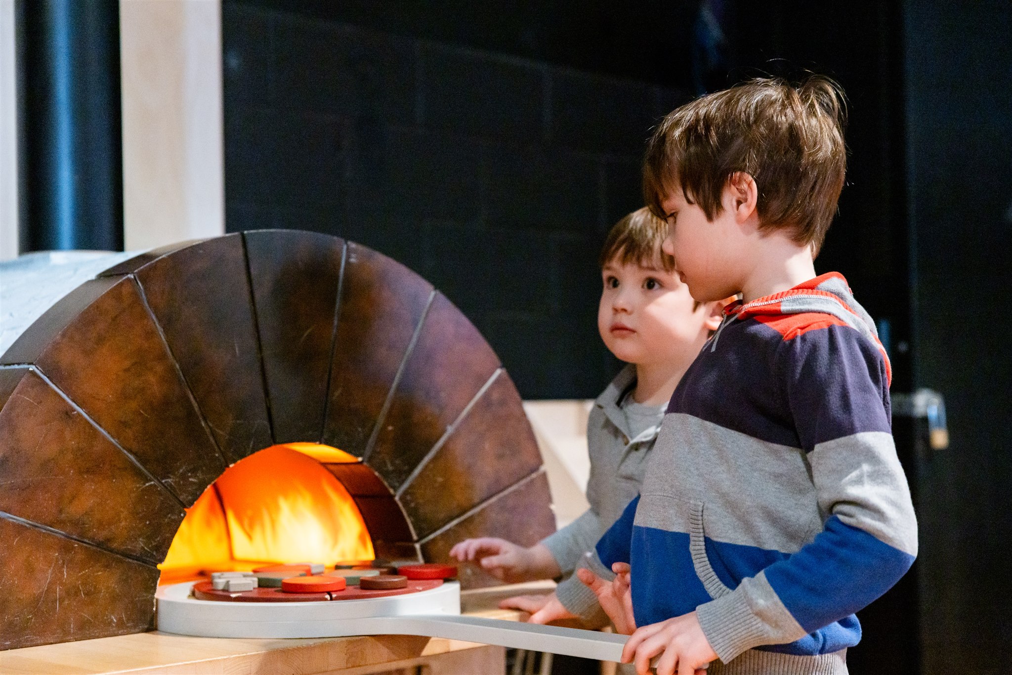 [Two boys playing with the pizza oven in KidSpark.][Deux garçons jouent avec le four à pizza dans l'espace KidSpark.]