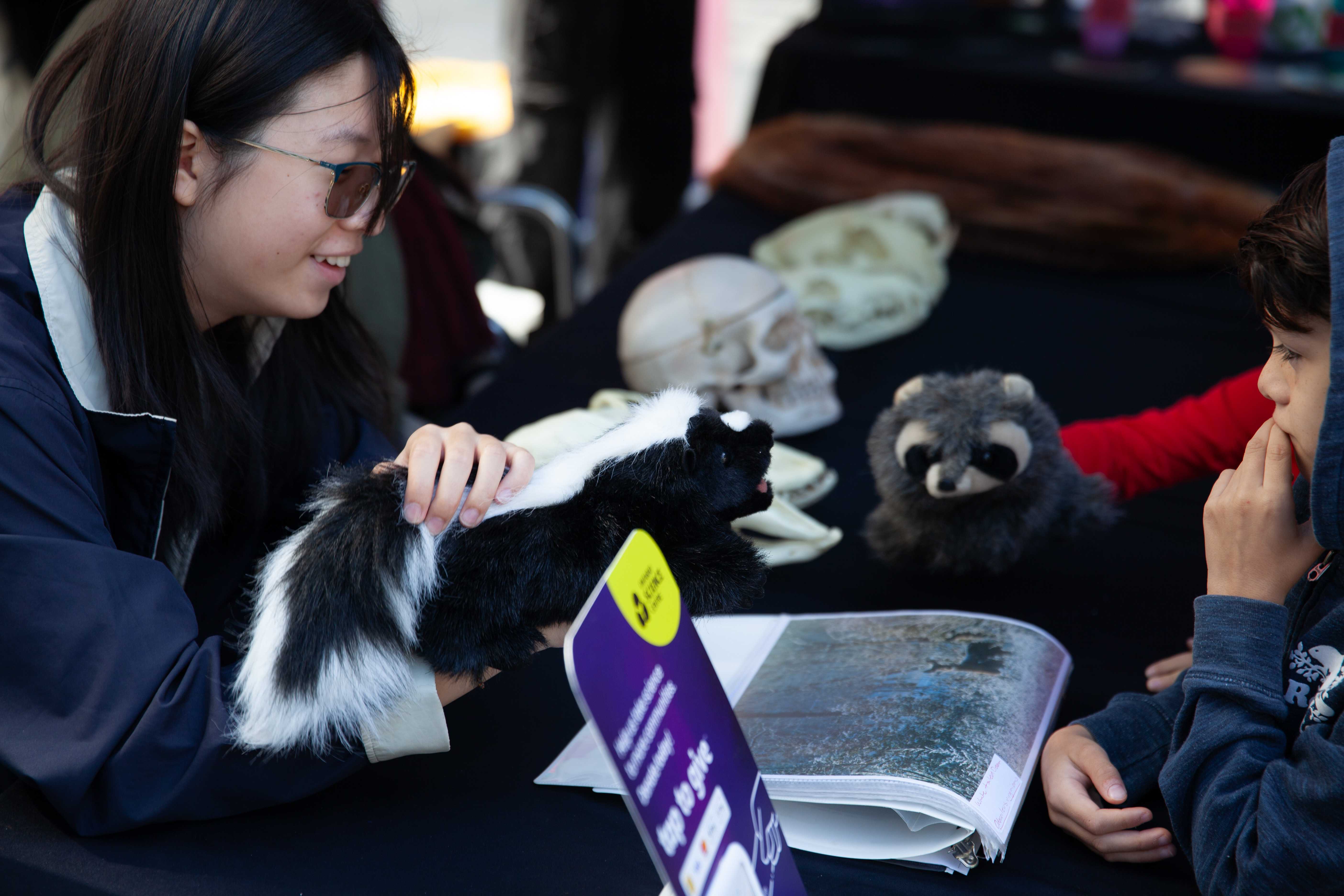 Two people play with a skunk and a racoon puppet.