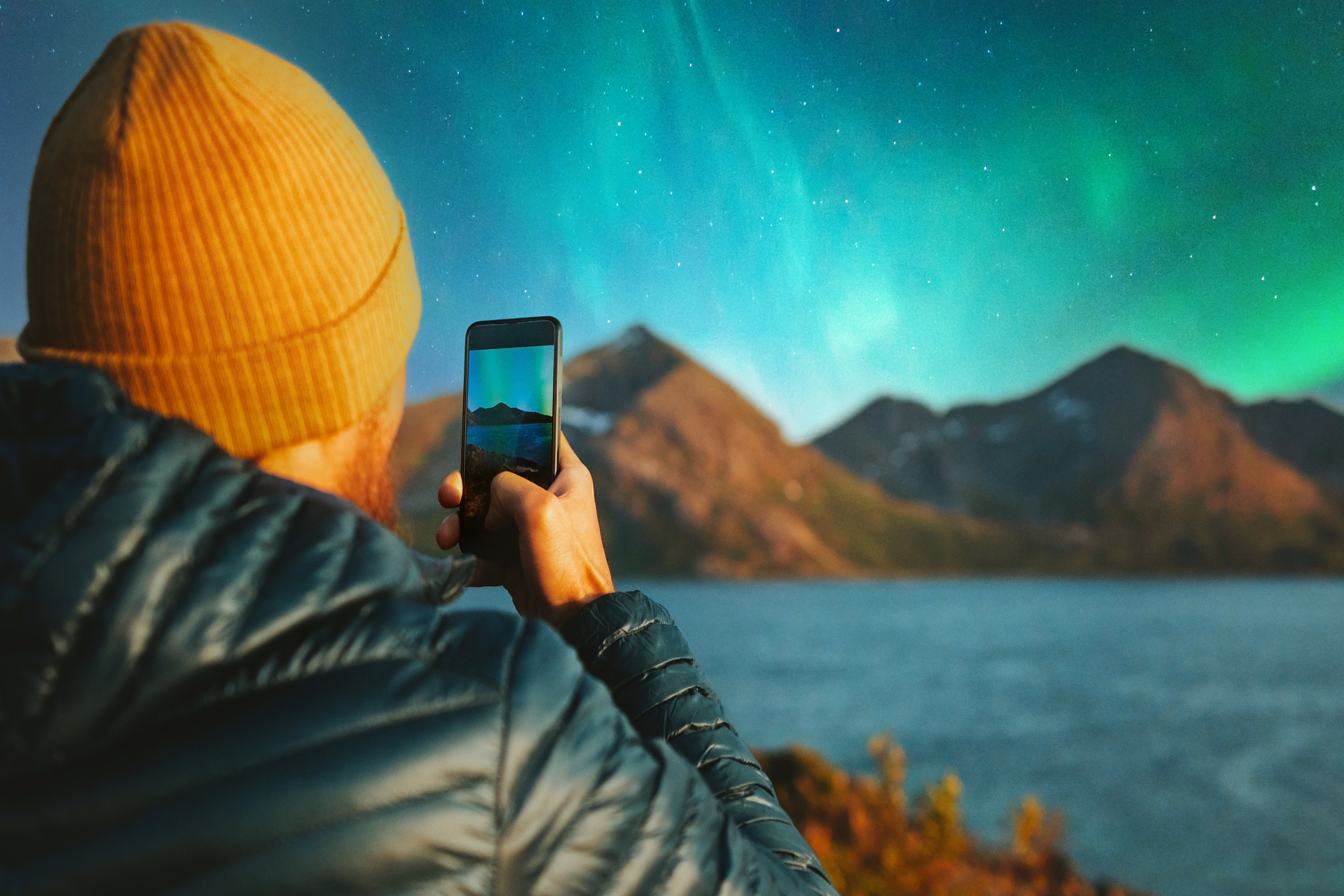 A man uses his smartphone to take a picture of the northern lights.