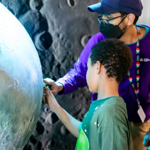 A science centre staff and a boy look at a display of the moon.