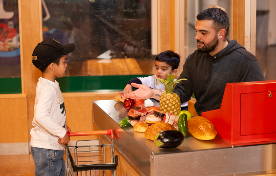 Father and his two sons playing at the cash counter with fruits and vegetables.