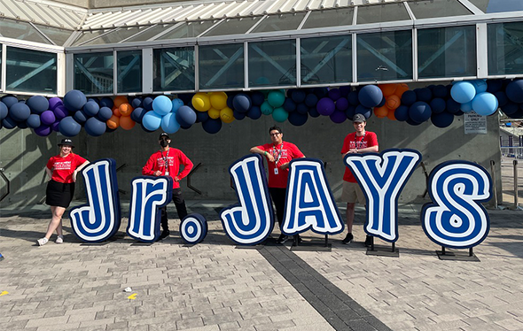 Four Ontario Science Centre Staff stand next to a Jr. Jays sign