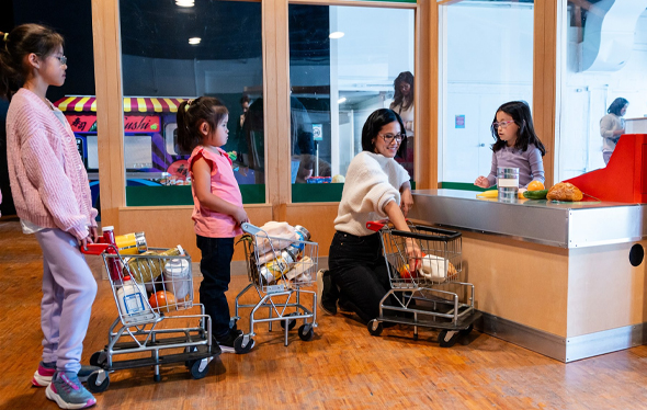 Two girls and a mom wait in line at the KidSpark grocery store.