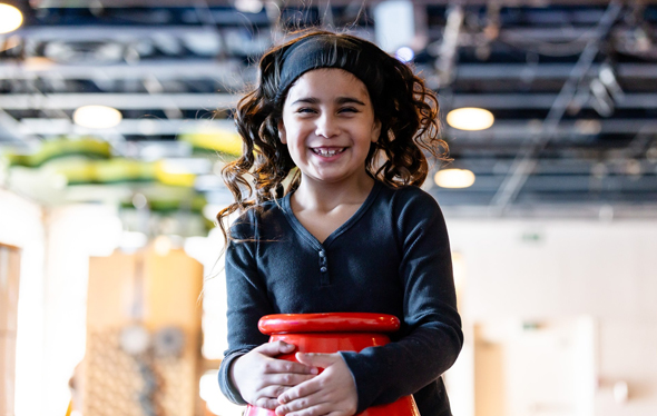 A young girl smiles at the camera, wind blowing her hair back.