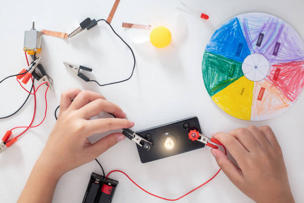 A child's hands use a circuit board to make a light bulb light up.