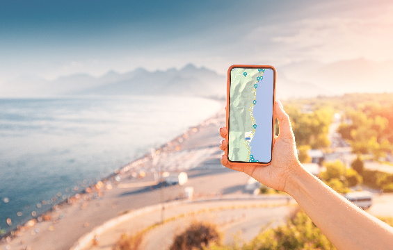 A hand holds a smartphone displaying landmarks on the landscape in the background.