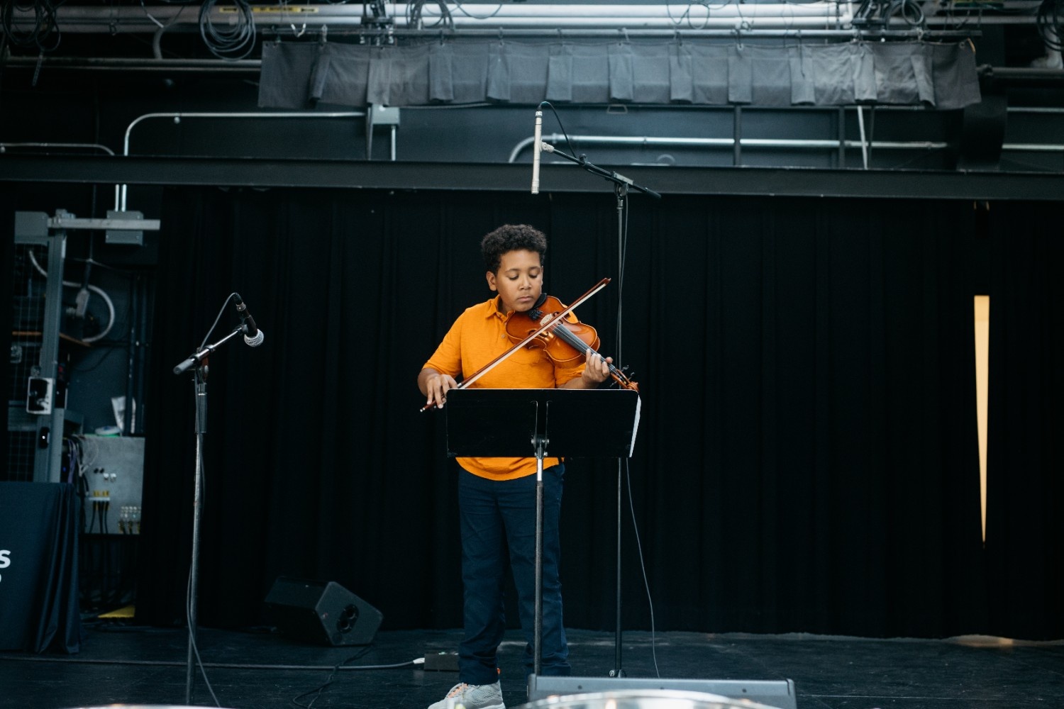 [A kid playing a violin on stage.][Un enfant jouant du violon sur scène.]