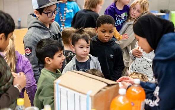 A group of children watch a bottle rocket experiment.