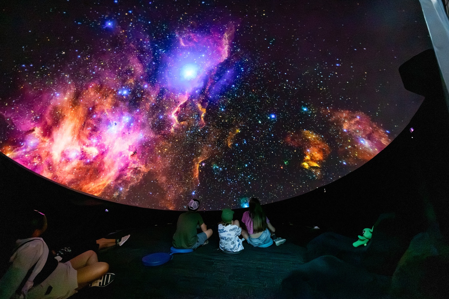[Kids sitting inside the planetarium dome watching the movie.][Des enfants assis sous le dôme du planétarium regardent le film.]
