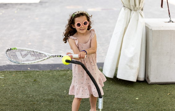 A little girl playing tennis with a racquet and ball.