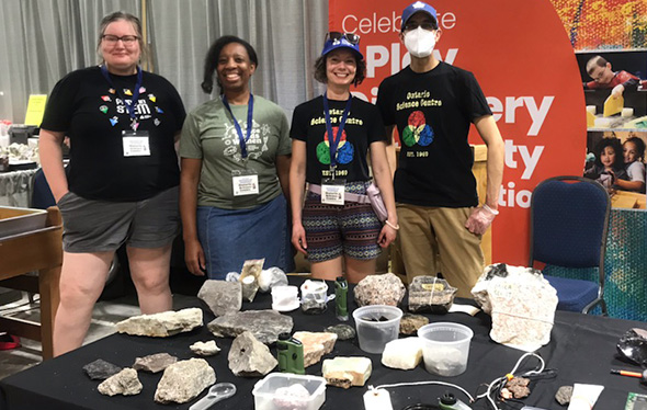 Four Ontario Science Centre staff stand with a table of display of rocks and minerals.