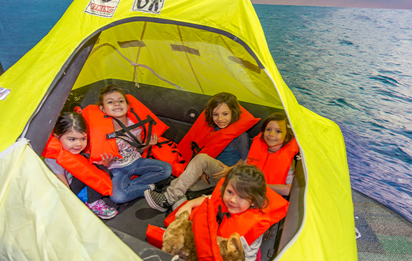 Five kids wearing life jackets sit in a raft.