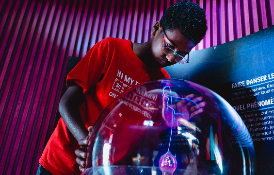 A young boy placing his hand on the plasma glass ball observing the electric spark touching his palm inside the ball.