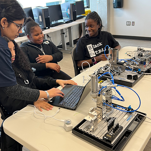 Four girls sit at a table with mechanical parts.