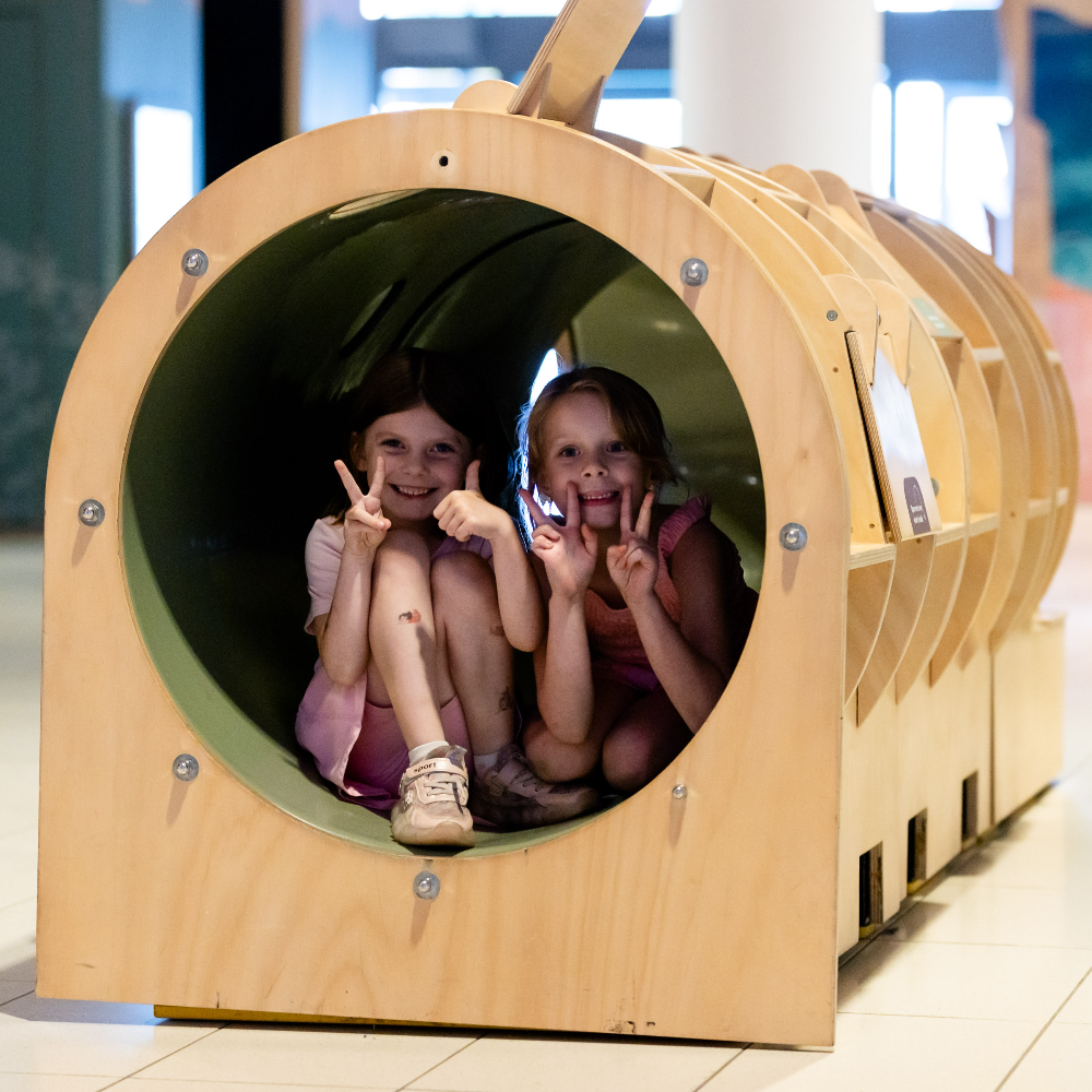 Two girls posing for a picture sitting inside a cylindrical exhibit.