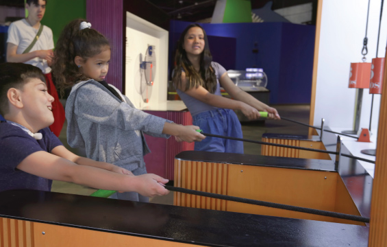 Three students pull on cords to lift weights with pulleys.