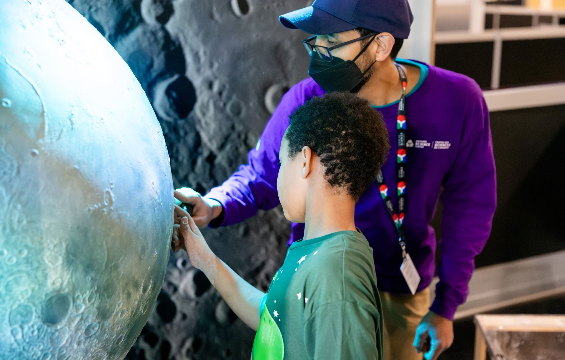 A science centre staff and a boy look at a display of the moon.