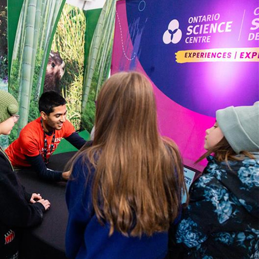 A science centre staff talks to a group of children.